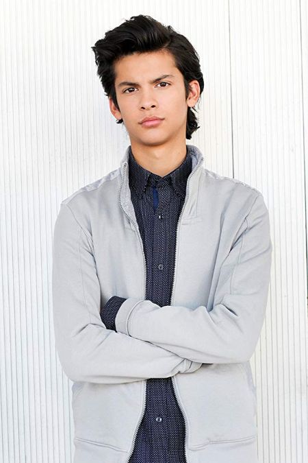Xolo Maridueña poses a picture in a grey coat.